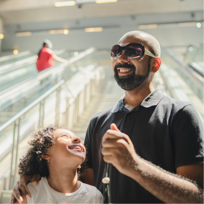 Blind man going down escalator next to child, both are smiling