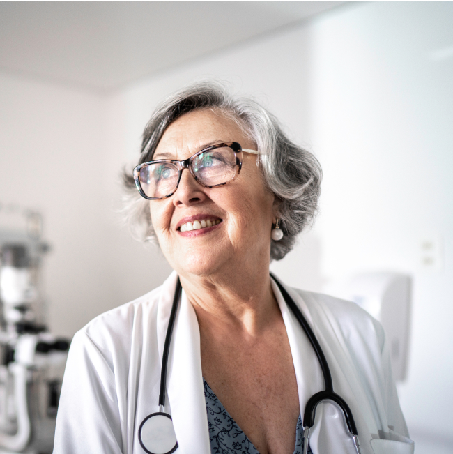 old woman in lab coat wearing glasses, smiling as she looks up