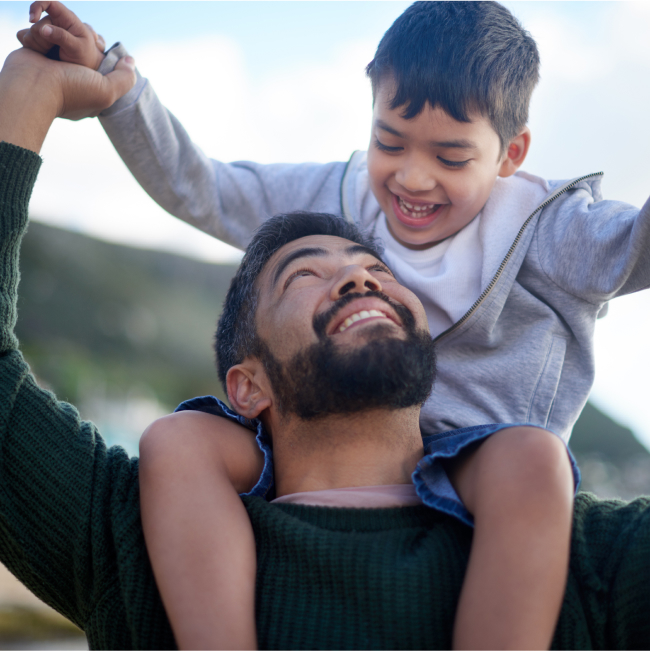 man holding child on his shoulder, looking up at the child and smiling