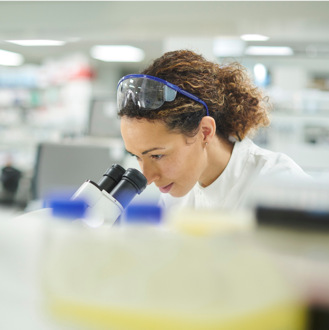 female researcher looking through microscope in a lab