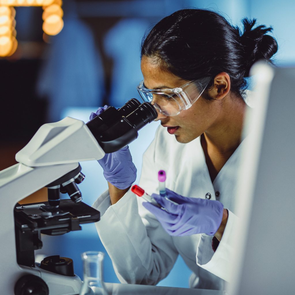 Researcher woman in lab coat looking through microscope